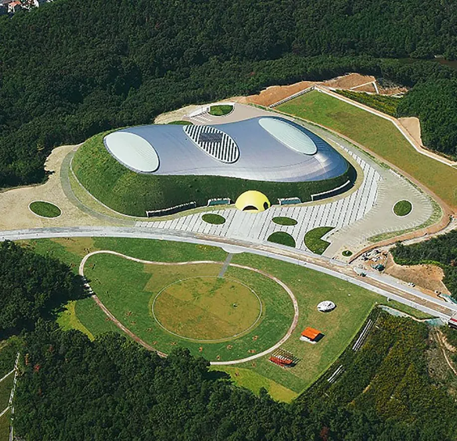 Flygbild över Bourbon Beans Dome i Miki City, Japan: ett välvt tak i en grön sluttning med en park runt omkring