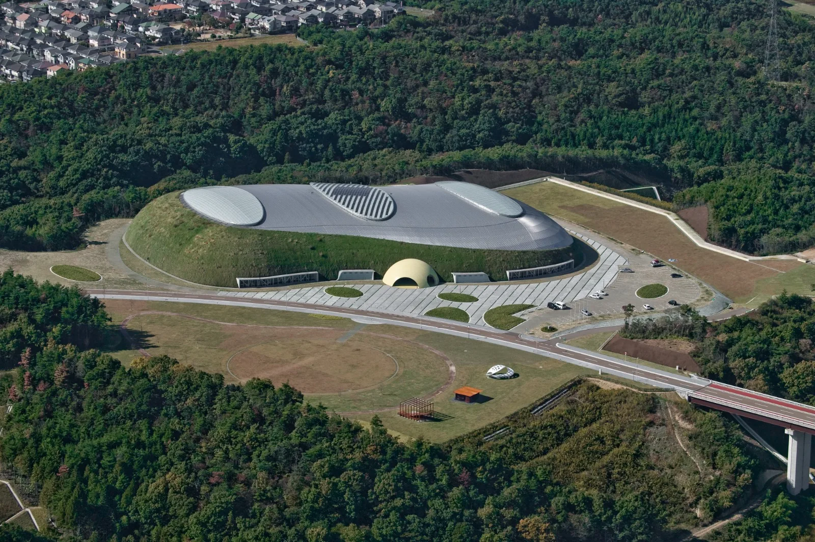 Aerial view of the Bourbon Beans Dome set into the forest landscape of Miki City, Japan, with its park and access road